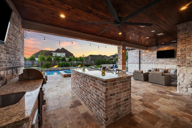 patio terrace at dusk featuring an outdoor hangout area, an outdoor bar, ceiling fan, and exterior kitchen