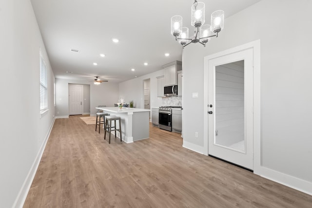 kitchen with backsplash, a kitchen island with sink, hanging light fixtures, appliances with stainless steel finishes, and a breakfast bar area