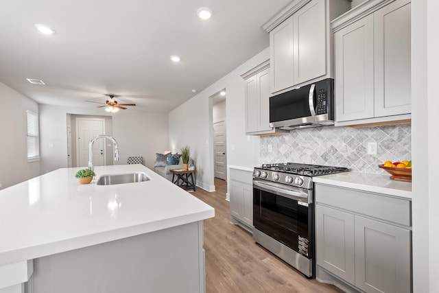 kitchen featuring gray cabinetry, sink, tasteful backsplash, a kitchen island with sink, and appliances with stainless steel finishes