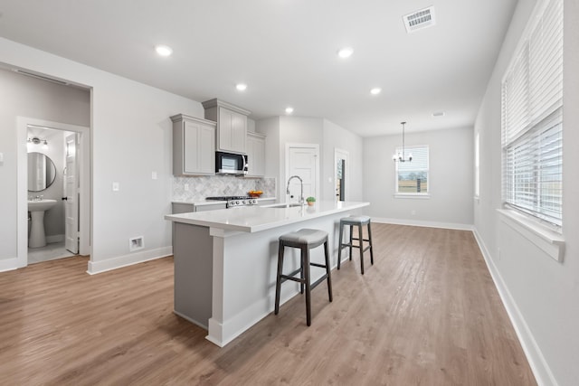 kitchen with a kitchen breakfast bar, light wood-type flooring, tasteful backsplash, gray cabinets, and an island with sink