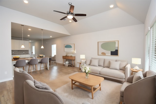 living room with ceiling fan, light hardwood / wood-style floors, sink, and vaulted ceiling