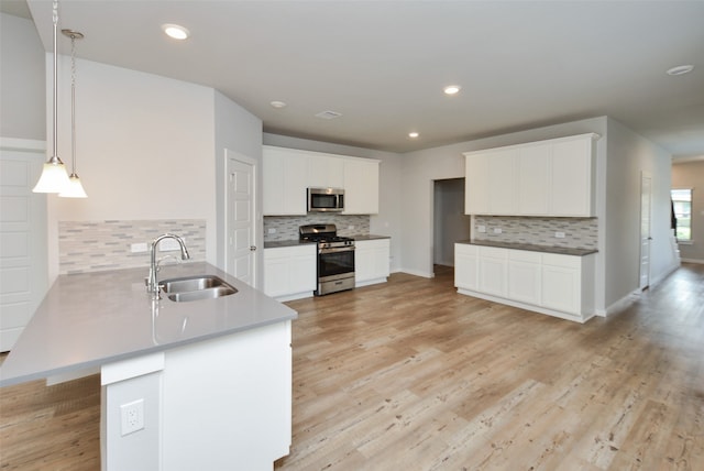 kitchen featuring kitchen peninsula, stainless steel appliances, sink, pendant lighting, and white cabinetry