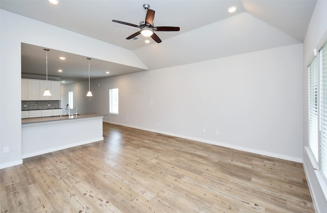 unfurnished living room with ceiling fan, sink, lofted ceiling, and light wood-type flooring