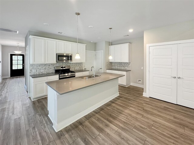 kitchen featuring white cabinets, stainless steel appliances, sink, pendant lighting, and an island with sink