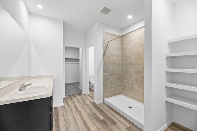 bathroom with toilet, a tile shower, wood-type flooring, and vanity