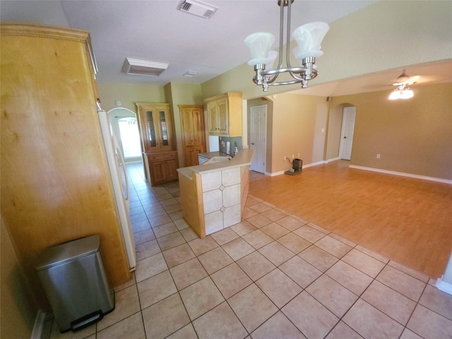 kitchen featuring sink, hanging light fixtures, kitchen peninsula, light tile patterned floors, and ceiling fan with notable chandelier