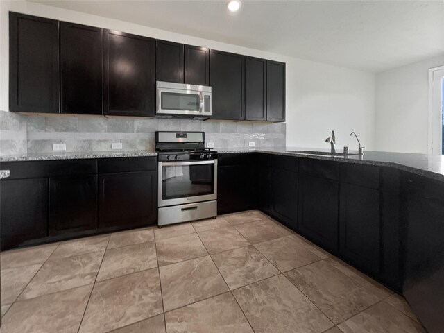 kitchen with stainless steel appliances, tasteful backsplash, light stone countertops, sink, and light tile floors