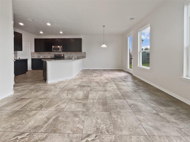 kitchen featuring light stone counters, kitchen peninsula, stove, pendant lighting, and backsplash