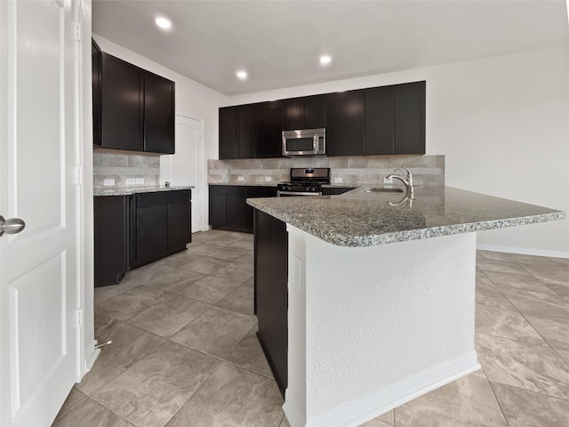 kitchen with sink, appliances with stainless steel finishes, kitchen peninsula, stone counters, and backsplash