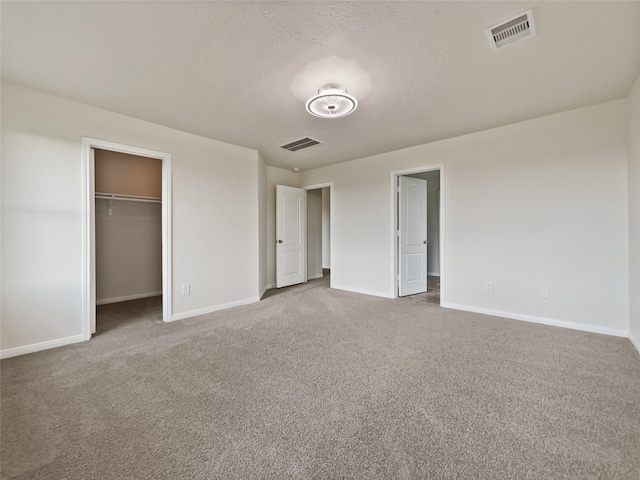 unfurnished bedroom featuring a walk in closet, a closet, a textured ceiling, and carpet flooring