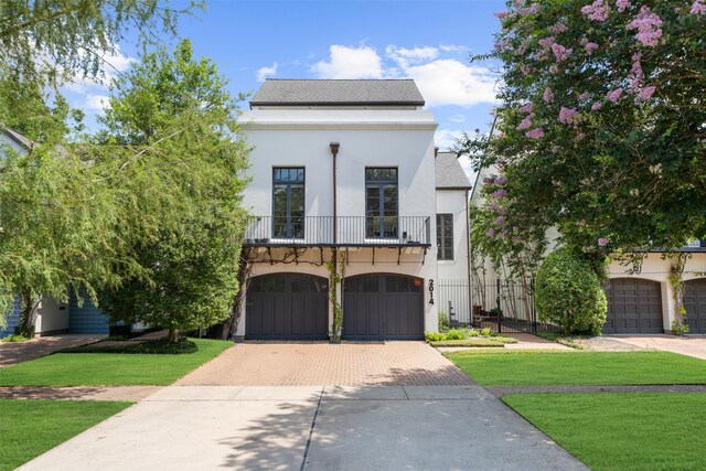 view of front of property featuring a garage, a balcony, and a front lawn