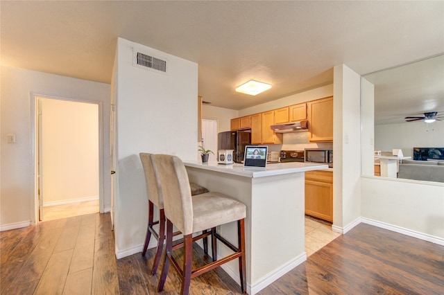 kitchen with kitchen peninsula, black refrigerator, a kitchen breakfast bar, and light brown cabinetry