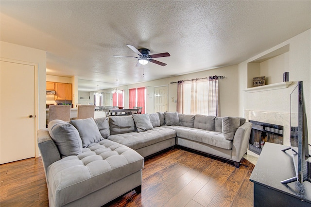 living room featuring a premium fireplace, ceiling fan, dark wood-type flooring, and a textured ceiling