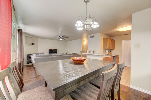 dining room with ceiling fan with notable chandelier, light hardwood / wood-style floors, and a tiled fireplace