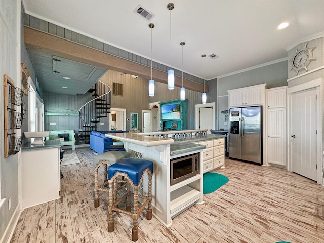 kitchen with appliances with stainless steel finishes, a kitchen island, white cabinetry, hanging light fixtures, and light hardwood / wood-style floors