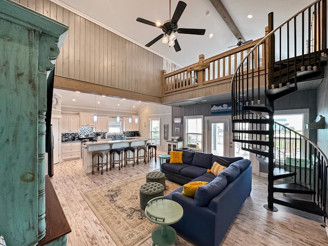 living room featuring light hardwood / wood-style floors, ceiling fan, crown molding, beam ceiling, and a high ceiling