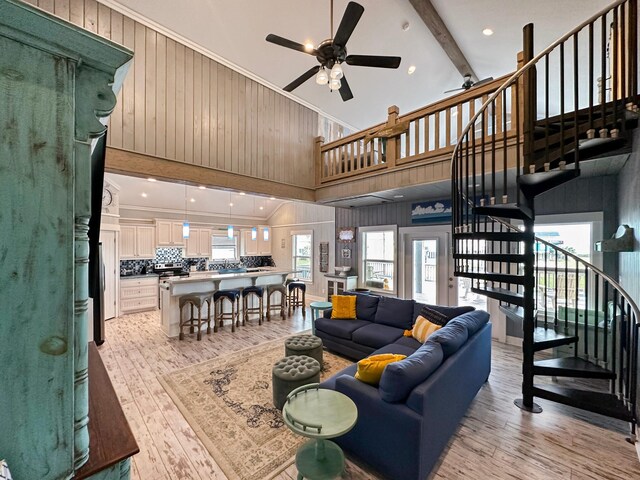 living room featuring ceiling fan, beam ceiling, wooden walls, high vaulted ceiling, and light hardwood / wood-style floors