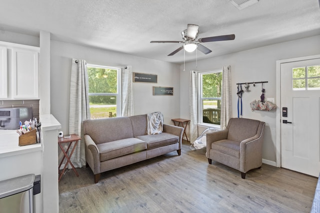 living room with ceiling fan, light wood-type flooring, a textured ceiling, and a wealth of natural light