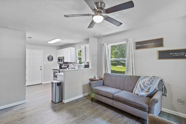 living room with a textured ceiling, ceiling fan, light hardwood / wood-style floors, and sink