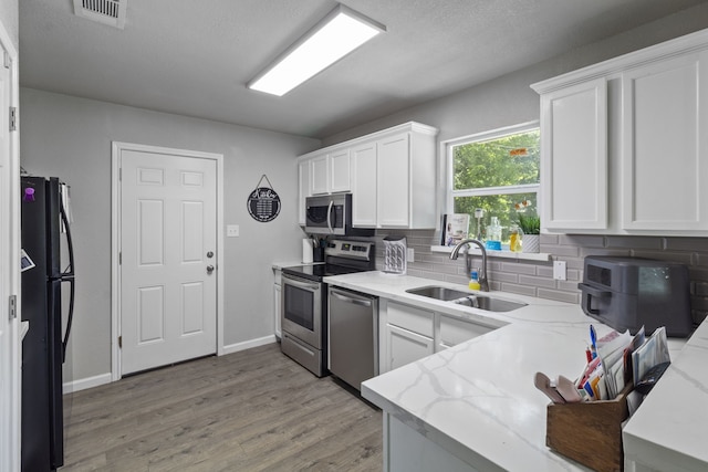 kitchen with light stone countertops, sink, stainless steel appliances, tasteful backsplash, and white cabinets