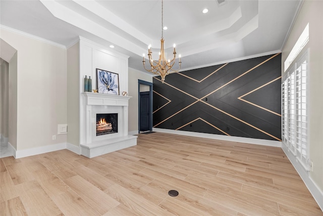 interior space with ornamental molding, a notable chandelier, light wood-type flooring, and a raised ceiling