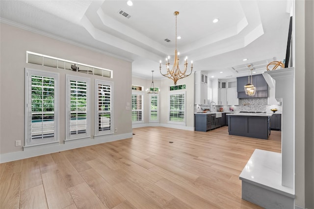 unfurnished living room with sink, a tray ceiling, crown molding, and light hardwood / wood-style flooring