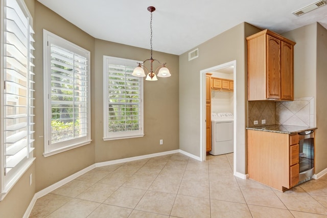 kitchen featuring backsplash, stone counters, an inviting chandelier, light tile patterned flooring, and washer / clothes dryer