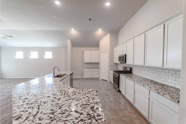 kitchen featuring light stone counters, tasteful backsplash, a center island with sink, white cabinetry, and stainless steel appliances