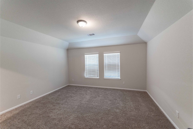 spare room featuring a textured ceiling, dark colored carpet, and vaulted ceiling