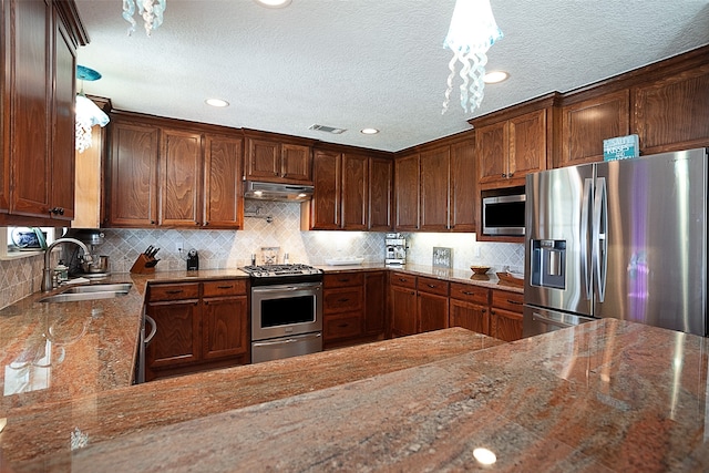 kitchen with sink, decorative backsplash, light stone countertops, hanging light fixtures, and appliances with stainless steel finishes