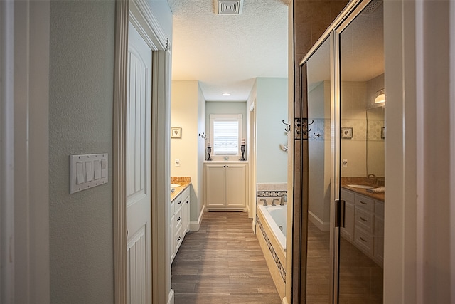 bathroom featuring shower with separate bathtub, hardwood / wood-style floors, vanity, and a textured ceiling