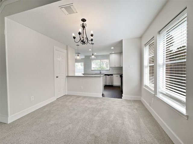 unfurnished living room with a healthy amount of sunlight, a chandelier, sink, and carpet flooring