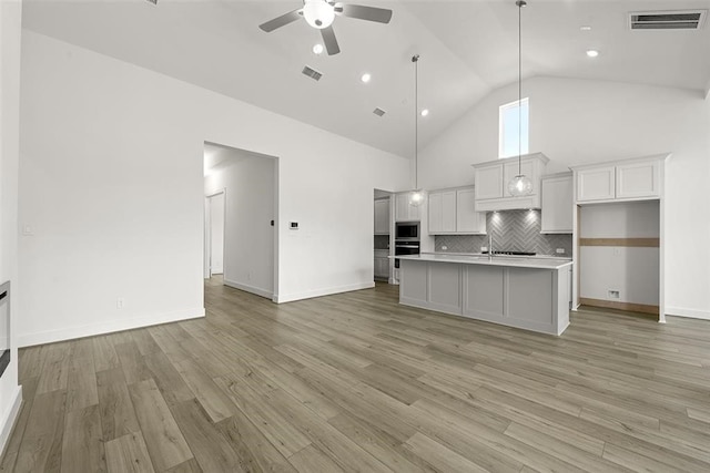 kitchen featuring light wood-type flooring, high vaulted ceiling, and decorative backsplash