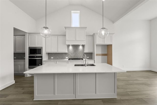 kitchen featuring backsplash, stainless steel appliances, sink, wood-type flooring, and a kitchen island with sink