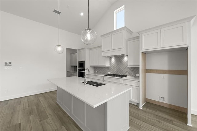 kitchen featuring wall oven, backsplash, light hardwood / wood-style floors, an island with sink, and white cabinetry