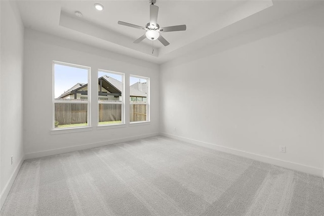 carpeted empty room featuring a raised ceiling, a wealth of natural light, and ceiling fan