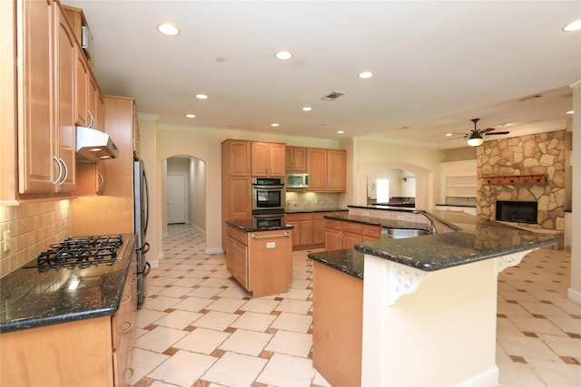 kitchen featuring ornamental molding, stainless steel appliances, ceiling fan, dark stone countertops, and a center island