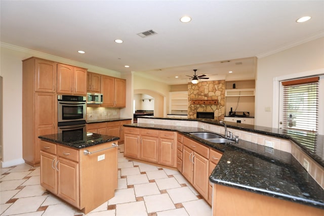 kitchen with ceiling fan, sink, stainless steel appliances, dark stone counters, and a center island with sink