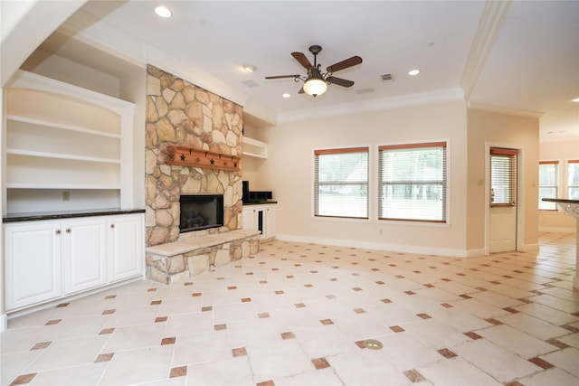 unfurnished living room featuring ceiling fan, a stone fireplace, built in features, and ornamental molding