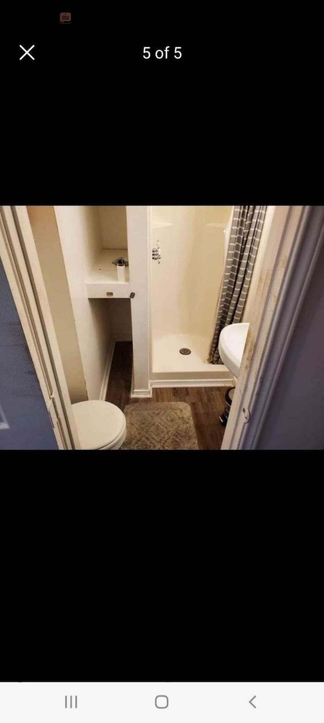 bathroom featuring walk in shower, toilet, and wood-type flooring