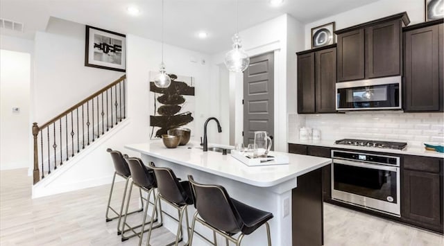 kitchen with tasteful backsplash, light wood-type flooring, pendant lighting, sink, and appliances with stainless steel finishes