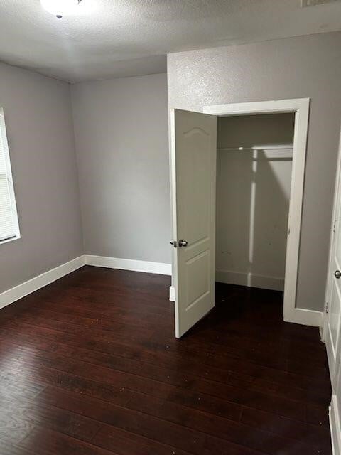 unfurnished bedroom with a textured ceiling, dark hardwood / wood-style floors, and a closet