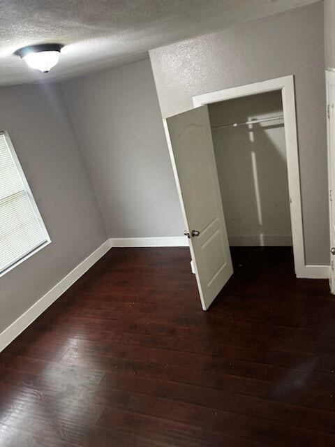 unfurnished bedroom with a textured ceiling, a closet, and dark wood-type flooring