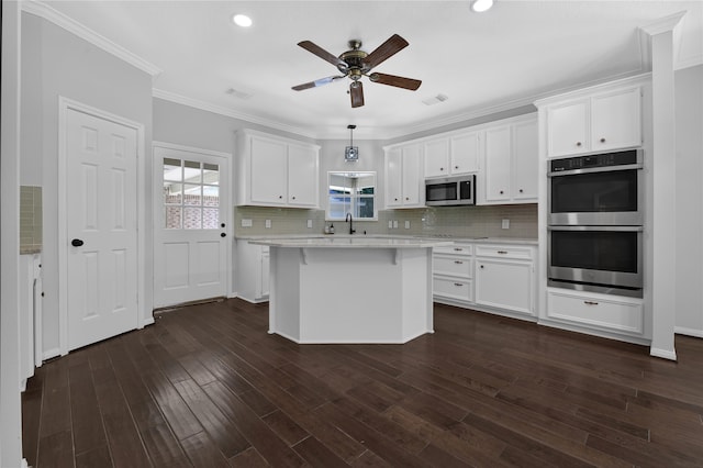 kitchen with white cabinetry, hanging light fixtures, dark wood-type flooring, stainless steel appliances, and ornamental molding