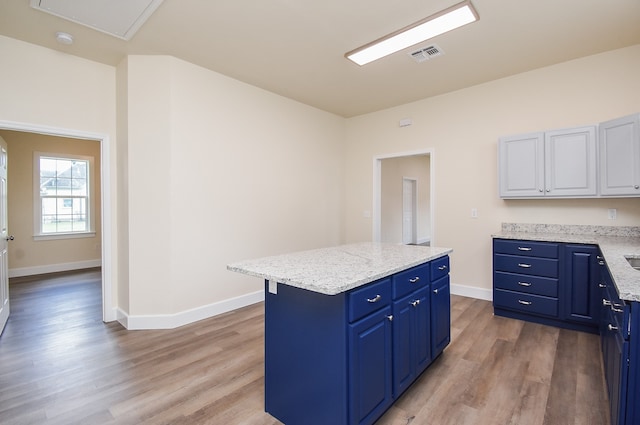 kitchen featuring light stone countertops, blue cabinetry, light hardwood / wood-style flooring, white cabinets, and a kitchen island