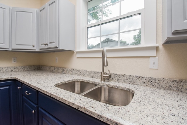 kitchen featuring white cabinets, light stone counters, sink, and blue cabinetry