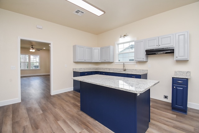 kitchen with ceiling fan, a kitchen island, light stone counters, light hardwood / wood-style floors, and white cabinets