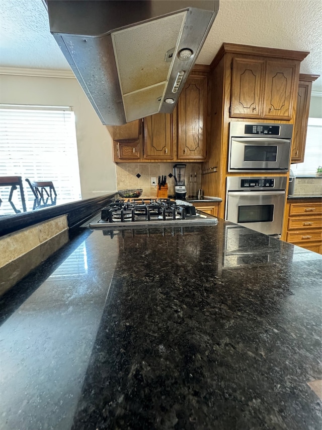 kitchen featuring a textured ceiling, appliances with stainless steel finishes, range hood, and ornamental molding