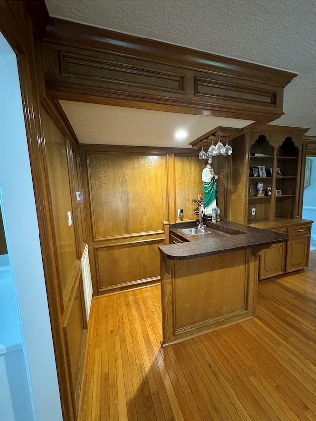 kitchen featuring wood walls, kitchen peninsula, sink, and light wood-type flooring