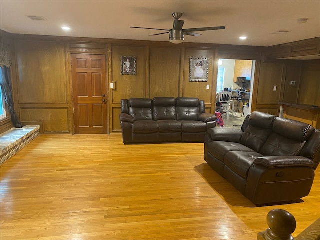 living room featuring ceiling fan, light wood-type flooring, and wood walls